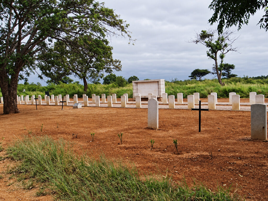 Peaceful cemetery in Bulawayo, Zimbabwe, with rows of simple white headstones and black crosses beneath mature trees and an overcast sky.