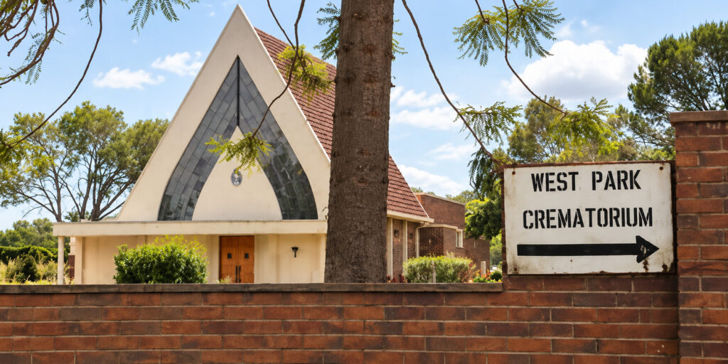 West Park Crematorium in Bulawayo, Zimbabwe, showing the chapel-style building behind a brick wall with a directional entrance sign.